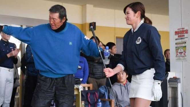 ゴルフ練習場で熱心な指導を受けているシーン