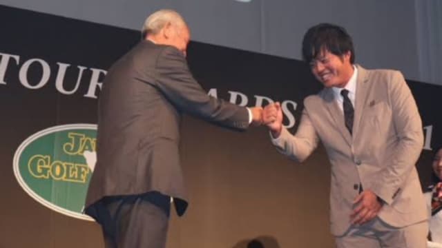 年間表彰式でJGTO会長の青木功からトロフィを授与されているイメージ画像